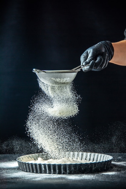 Vue de face femme cuisinier versant de la farine blanche dans la casserole sur la pâte noire travail d'oeuf boulangerie hotcake cuisine cuisine