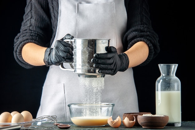 Vue de face femme cuisinier versant de la farine dans une assiette avec des œufs pour la pâte sur la pâtisserie sombre gâteau tarte travailleur cuisine travail pâte à hotcake