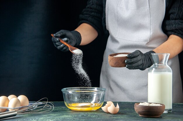 Vue de face femme cuisinier versant de la farine dans les œufs pour la pâte sur la pâtisserie foncée gâteau tarte travailleur pâte à gâteau cuisine emploi boulangerie