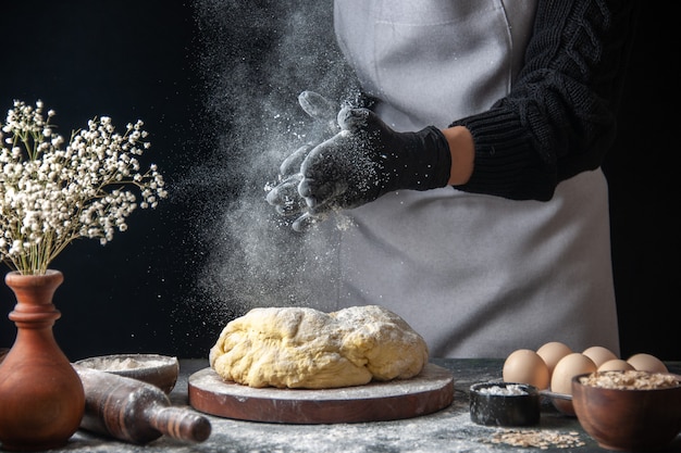 Vue de face femme cuisinière étaler la pâte avec de la farine sur un travail sombre four à tarte de boulangerie de pâtisserie de pâte crue