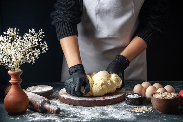 Vue de face femme cuisinière étaler la pâte sur un travail de pâtisserie sombre pâte crue boulangerie hotcake four à tartes