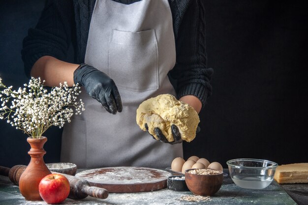 Vue de face femme cuisinière étaler la pâte sur un travail sombre four à tarte à pâte crue œuf de boulangerie