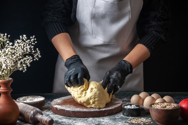 Vue de face femme cuisinière étaler la pâte sur un travail sombre pâte crue boulangerie pâtisserie tarte au four