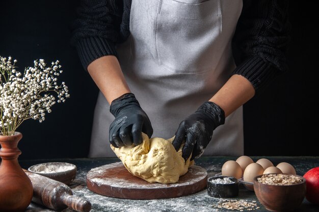 Vue de face femme cuisinière étaler la pâte sur un travail sombre pâte crue boulangerie pâtisserie tarte au four