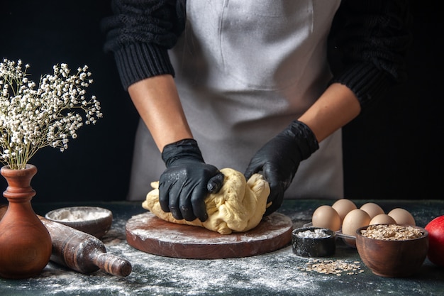 Vue de face femme cuisinière étaler la pâte sur un travail sombre pâte crue boulangerie pâtisserie tarte au four