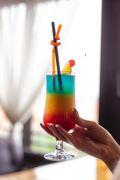 Vue de face femme détient un cocktail multicolore avec une tranche d'orange