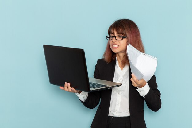 Vue de face femme employé de bureau en costume strict tenant à l'aide d'un ordinateur portable sur une surface bleue