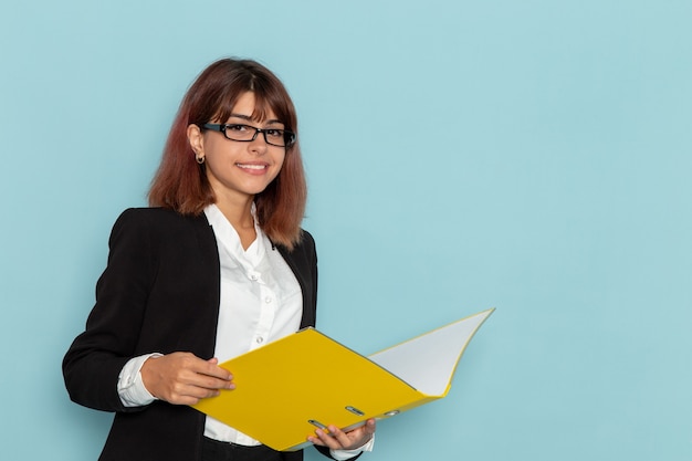 Vue de face femme employé de bureau lisant et tenant le fichier jaune sur la surface bleue