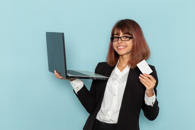Vue de face femme employé de bureau tenant carte et ordinateur portable sur la surface bleue