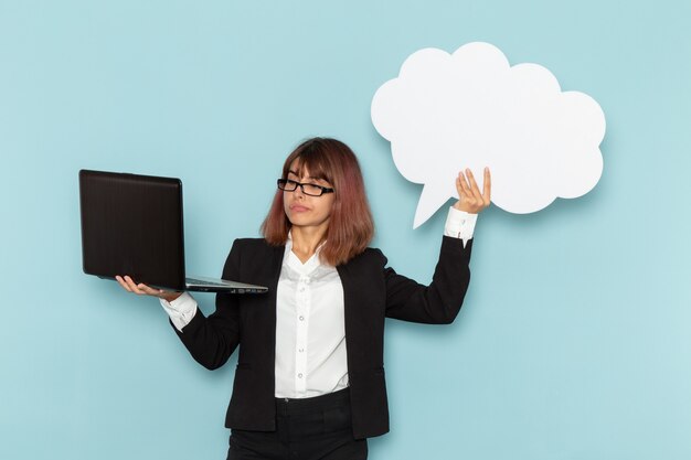 Vue de face femme employé de bureau tenant grand panneau blanc et ordinateur portable sur la surface bleue