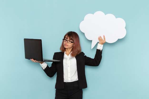 Vue de face femme employé de bureau tenant une pancarte blanche et un ordinateur portable sur la surface bleu clair