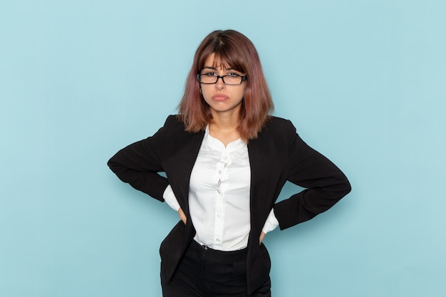 Vue de face femme employé de bureau en veste noire avec une expression stressée sur la surface bleue