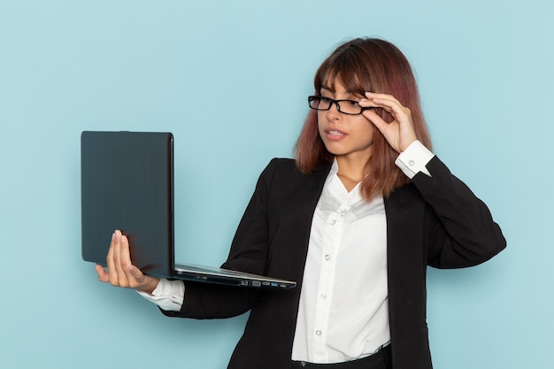 Vue de face femme employée de bureau en costume strict à l'aide d'un ordinateur portable sur une surface bleue