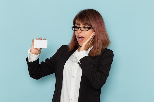 Vue de face femme employée de bureau en costume strict tenant une carte blanche sur la surface bleue