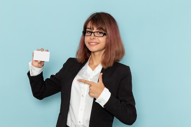 Vue de face femme employée de bureau en costume strict tenant une carte en plastique blanc sur une surface bleue