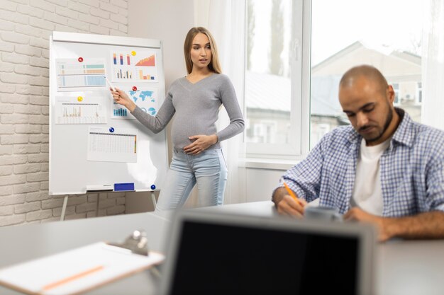 Vue de face de la femme enceinte donnant une présentation tandis qu'un collègue prend des notes