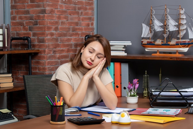 Vue de face d'une femme endormie mettant la tête sur les mains jointes travaillant au bureau