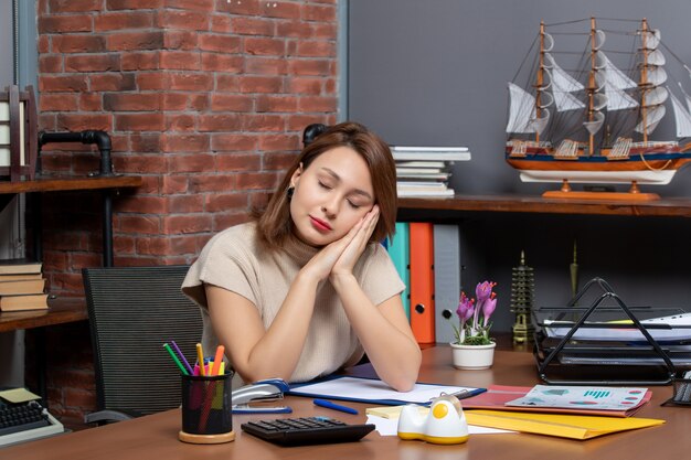 Vue de face d'une femme endormie mettant la tête sur les mains jointes travaillant au bureau