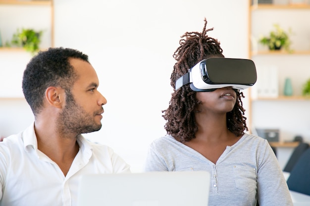 Vue de face d'une femme excitée testant un casque VR avec un assistant