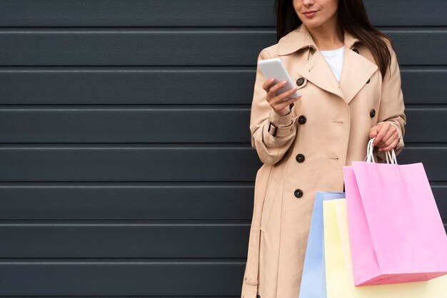 Vue de face de la femme à l'extérieur à la recherche de smartphone tout en holing sacs