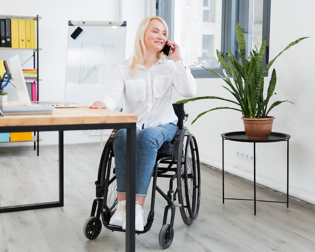 Vue de face de femme en fauteuil roulant, parler au téléphone au travail