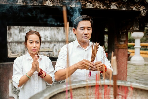 Vue de face de la femme et de l'homme priant au temple avec de l'encens brûlant