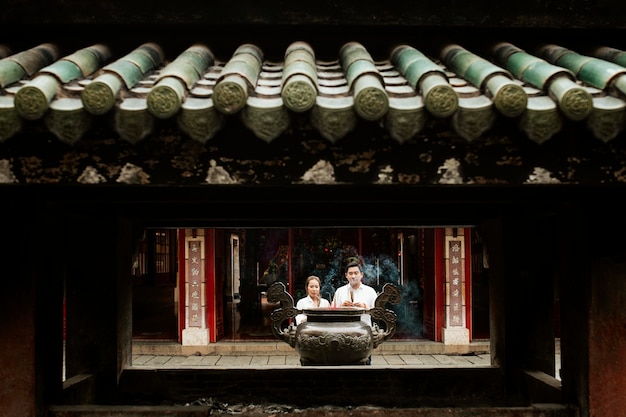 Vue de face de la femme et de l'homme priant au temple avec de l'encens brûlant