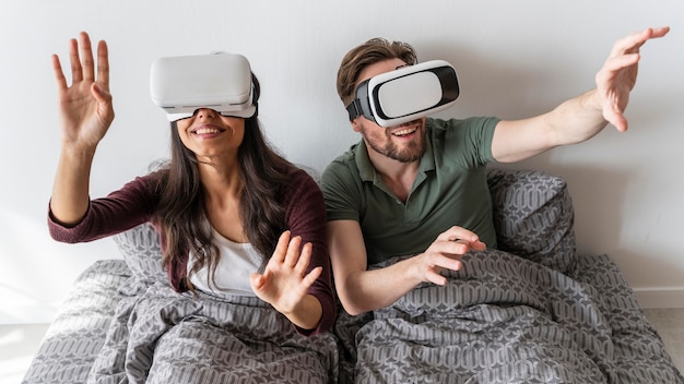 Vue de face de la femme et de l'homme smiley à l'aide d'un casque de réalité virtuelle au lit