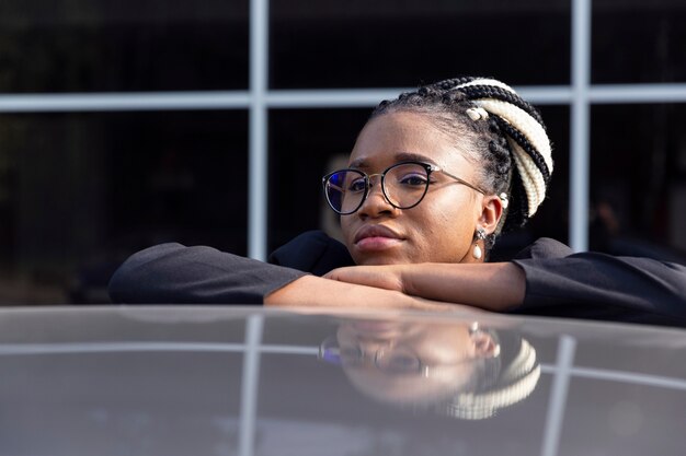 Vue de face de la femme avec des lunettes reposant sa tête sur le dessus de la voiture