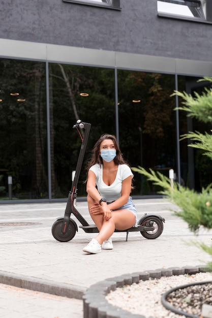 Vue de face de la femme avec masque médical et scooter à l'extérieur