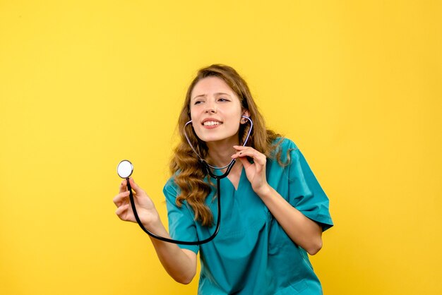 Vue de face femme médecin à l'aide d'un stéthoscope sur l'espace jaune