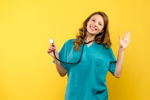 Vue de face de la femme médecin à l'aide d'un stéthoscope sur mur jaune