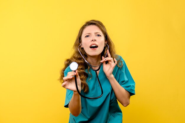 Vue de face de la femme médecin à l'aide d'un stéthoscope sur mur jaune