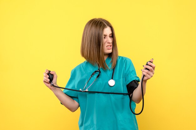 Vue de face femme médecin à l'aide de tonomètre sur l'espace jaune clair