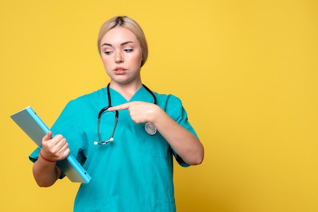 Vue de face de la femme médecin avec analyse et stéthoscope sur mur jaune