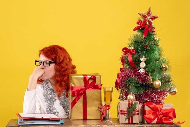 Vue de face femme médecin assis avec des cadeaux de Noël et arbre sur fond jaune