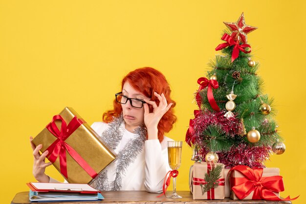 Vue de face femme médecin assis avec des cadeaux de Noël et arbre sur fond jaune