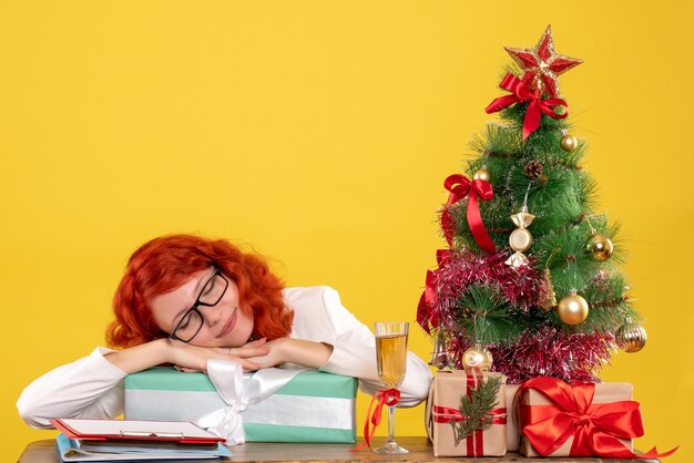 Vue de face femme médecin assis avec des cadeaux de Noël et arbre sur fond jaune