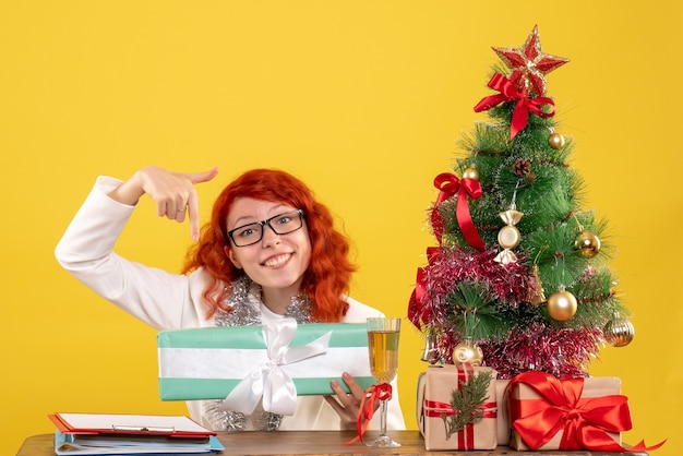 Vue de face femme médecin assis avec des cadeaux de Noël sur fond jaune