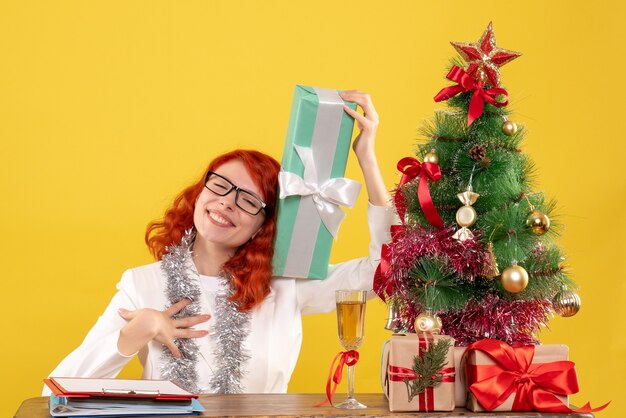 Vue de face femme médecin assis avec des cadeaux de Noël sur fond jaune