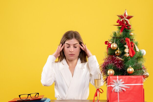 Vue de face femme médecin assis devant sa table sur le fond jaune