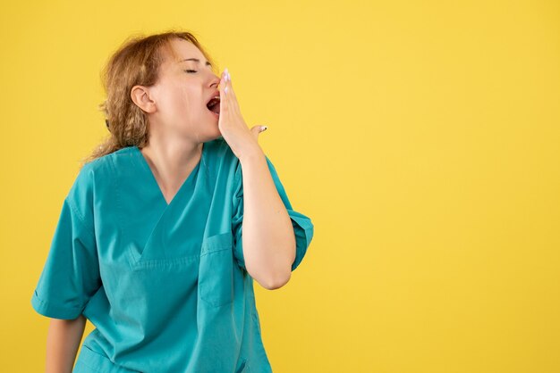 Vue de face de la femme médecin en chemise médicale bâillements sur mur jaune