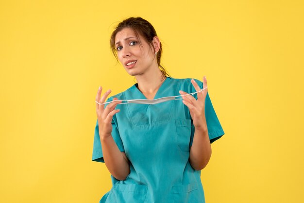 Vue de face femme médecin en chemise médicale décoller masque stérile sur fond jaune