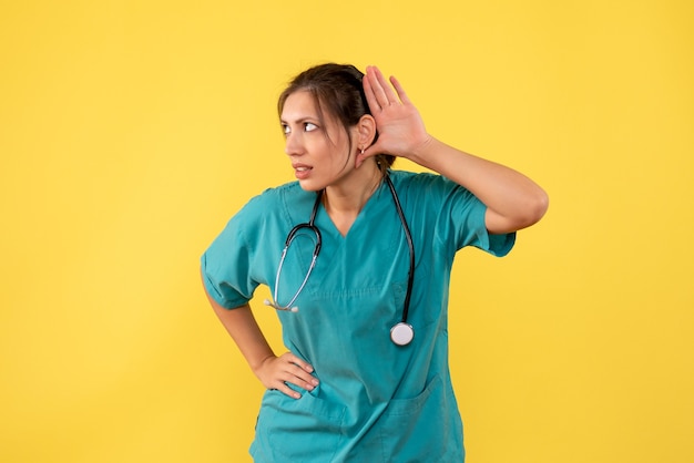 Vue de face femme médecin en chemise médicale à l'écoute sur fond jaune