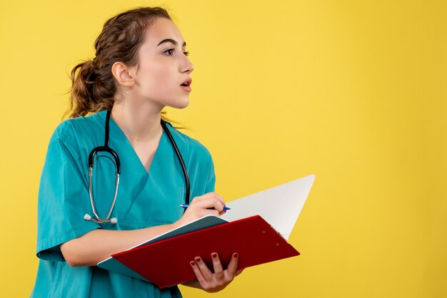 Vue de face de la femme médecin en chemise médicale, écrire des notes sur le mur jaune