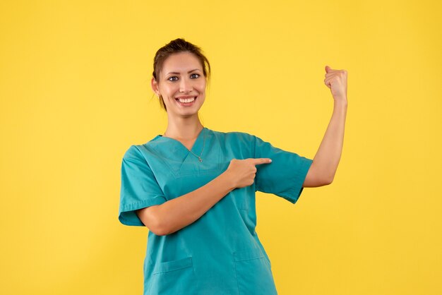 Vue de face femme médecin en chemise médicale fléchissant sur fond jaune