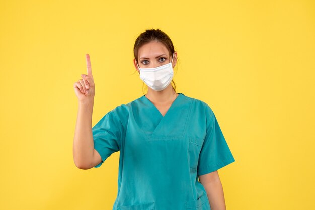 Vue de face femme médecin en chemise médicale et masque sur fond jaune