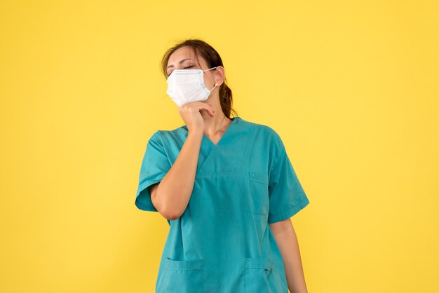 Vue de face femme médecin en chemise médicale et masque sur fond jaune