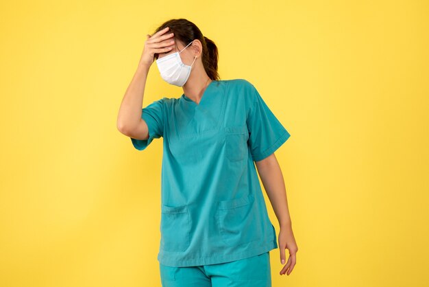 Vue de face femme médecin en chemise médicale et masque avec maux de tête sur fond jaune