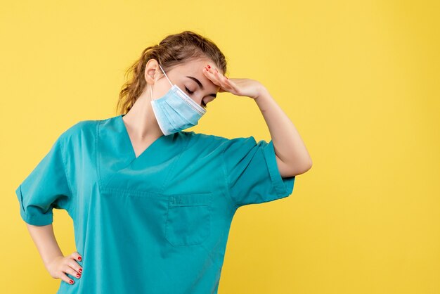 Vue de face femme médecin en chemise médicale et masque stérile sur bureau jaune couleur pandémique uniforme de santé virus covid-19